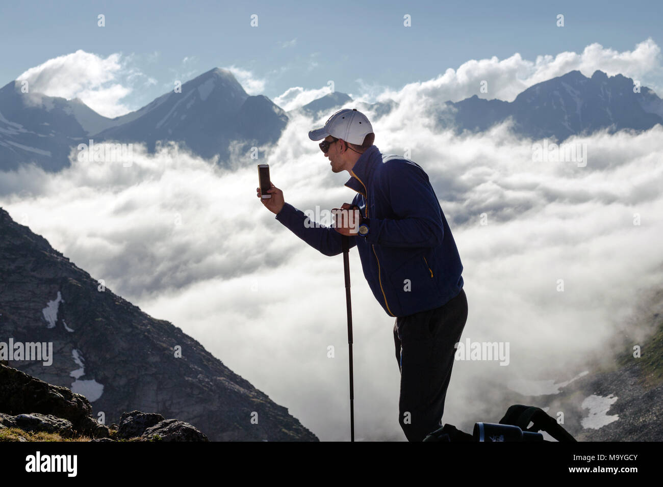 Hipster homme tire une vidéo d'un paysage de montagne avec des nuages sur un téléphone mobile, alors que l'article de fond contre les hauts sommets. L'homme est tak Banque D'Images