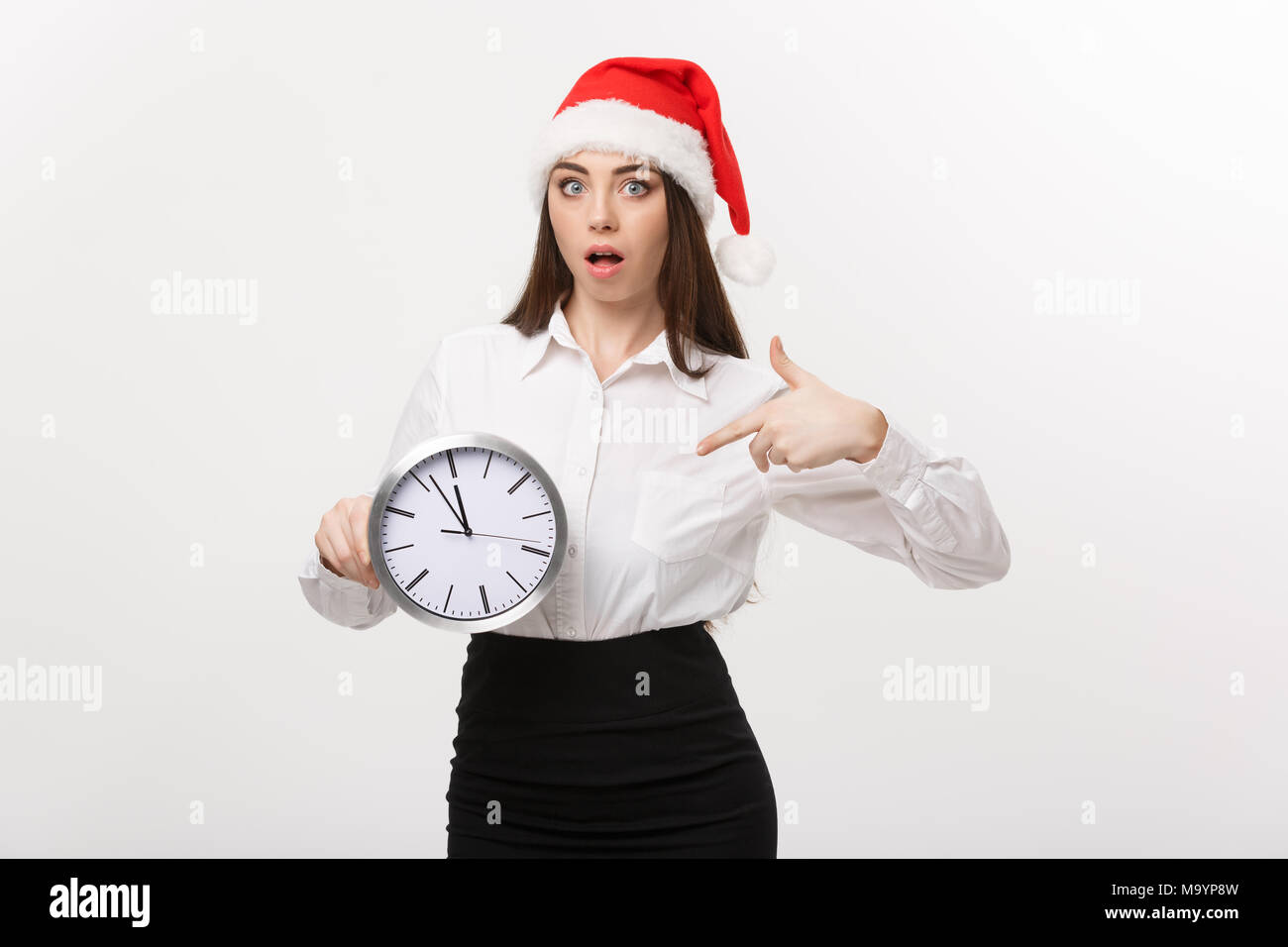 Concept de gestion du temps - Young business woman with santa hat holding et de pointage d'une horloge isolated over white background. Banque D'Images