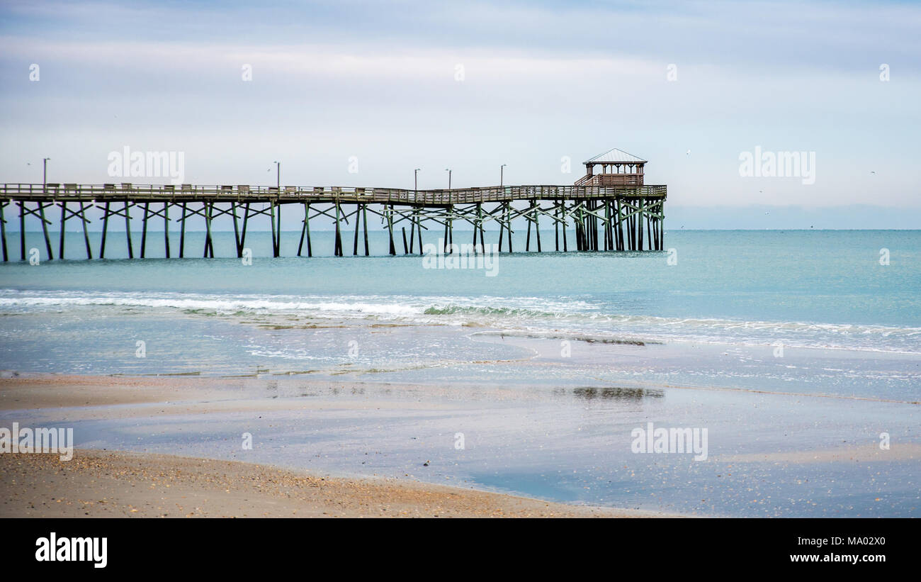 Lever du soleil avec l'Atlantic Beach Pier dans l'arrière-plan avec du sable, de l'océan, des vagues et des nuages bleus Banque D'Images