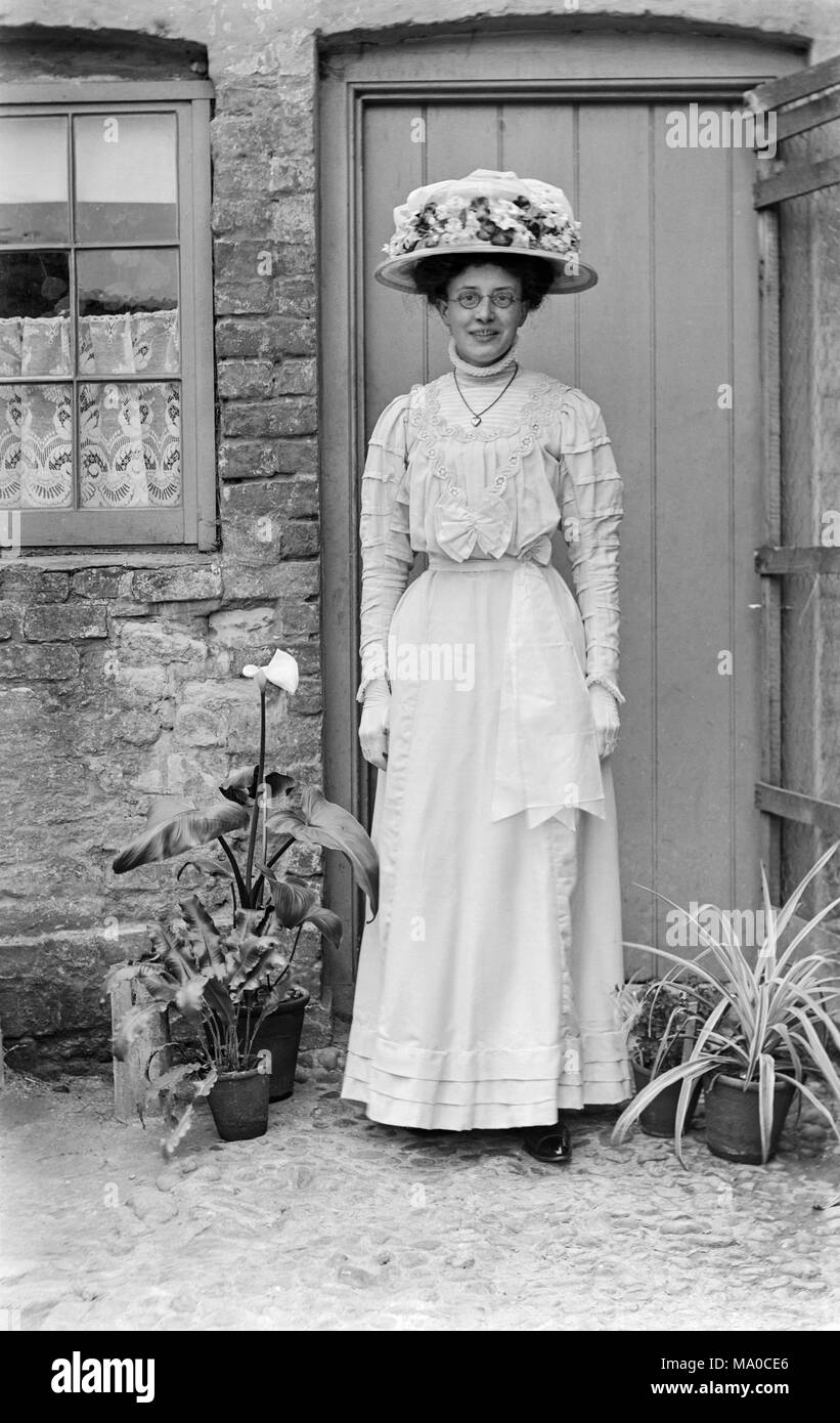 Jeune femme vêtue comme une demoiselle à la fin de l'Angleterre Victorienne. Elle porte des lunettes rondes, et est habillé entièrement en blanc, avec un chapeau à fleurs blanches. Banque D'Images