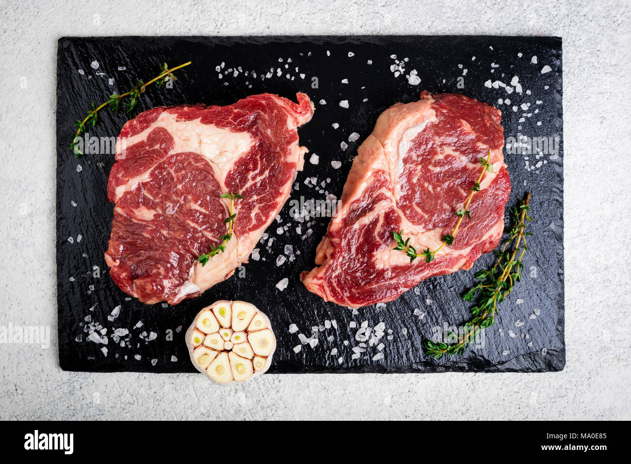 La viande crue. Steak de boeuf sur une planche à découper, de romarin et d'épices, vue d'en haut. La cuisson des viandes Banque D'Images