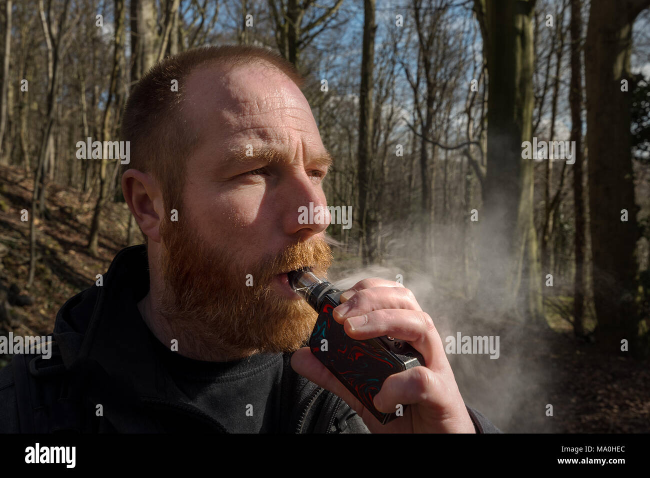 Un homme barbu vapes gingembre sur une case mod avec vaporisateur en verre. Banque D'Images