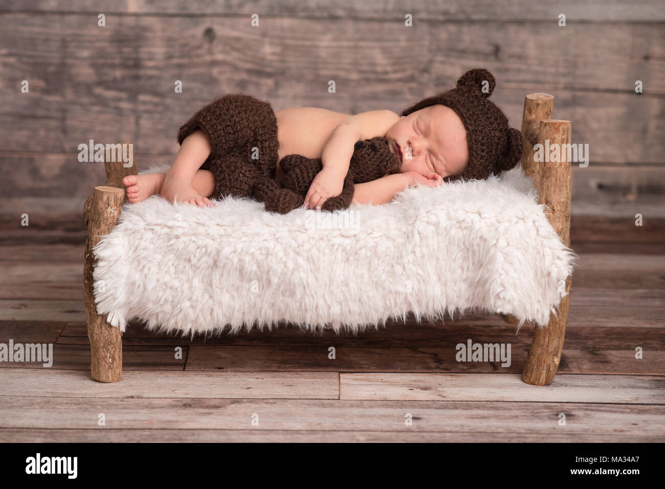 Deux semaines de bébé nouveau-né garçon portant un ours brun, moufles,  bonnet. Il est en train de dormir sur un petit lit en bois, et de câliner  un animal en peluche Photo