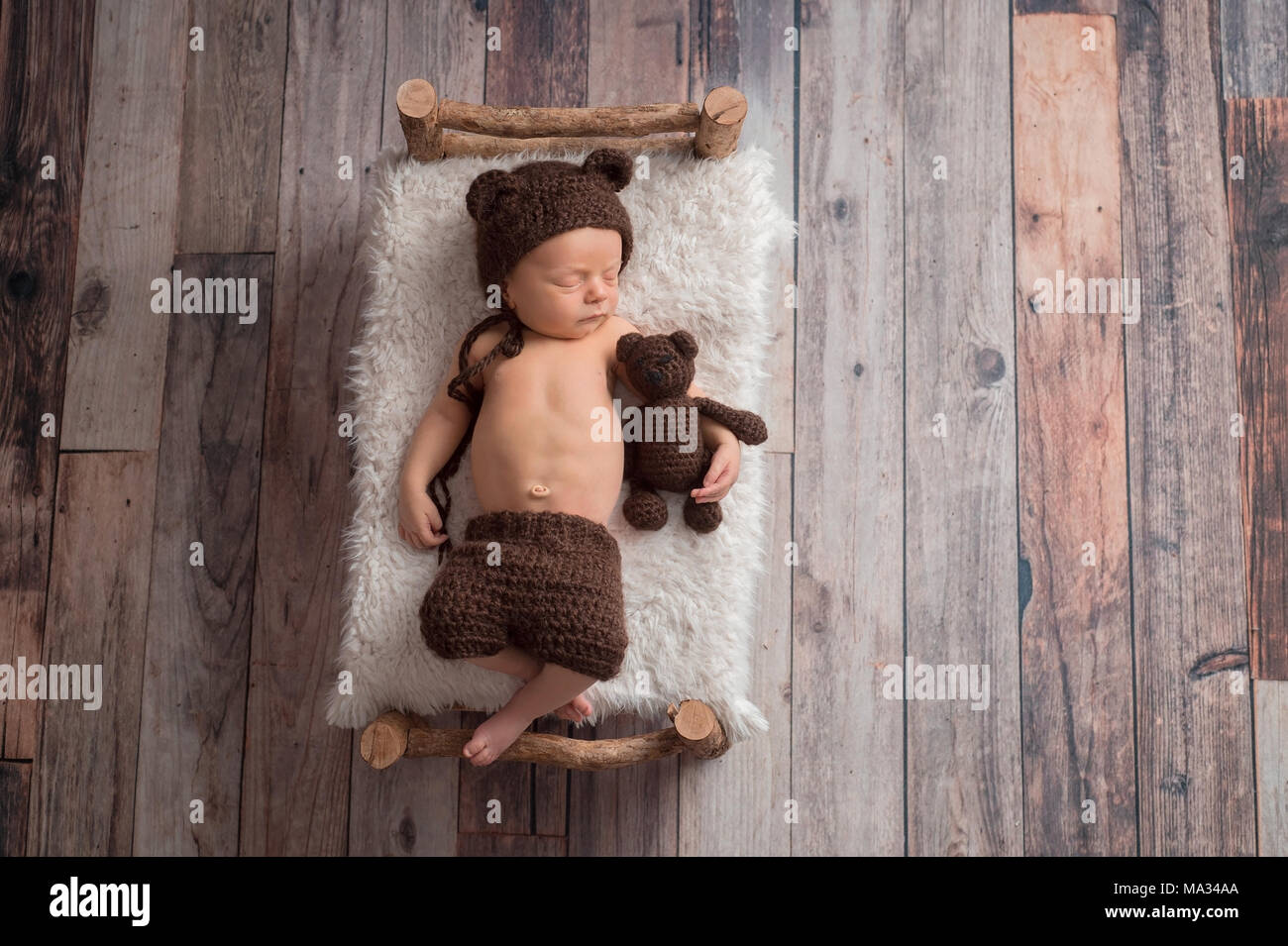 Deux semaines de bébé nouveau-né garçon portant un ours brun, moufles,  bonnet. Il est en train de dormir sur un petit lit en bois, et de câliner  un animal en peluche Photo