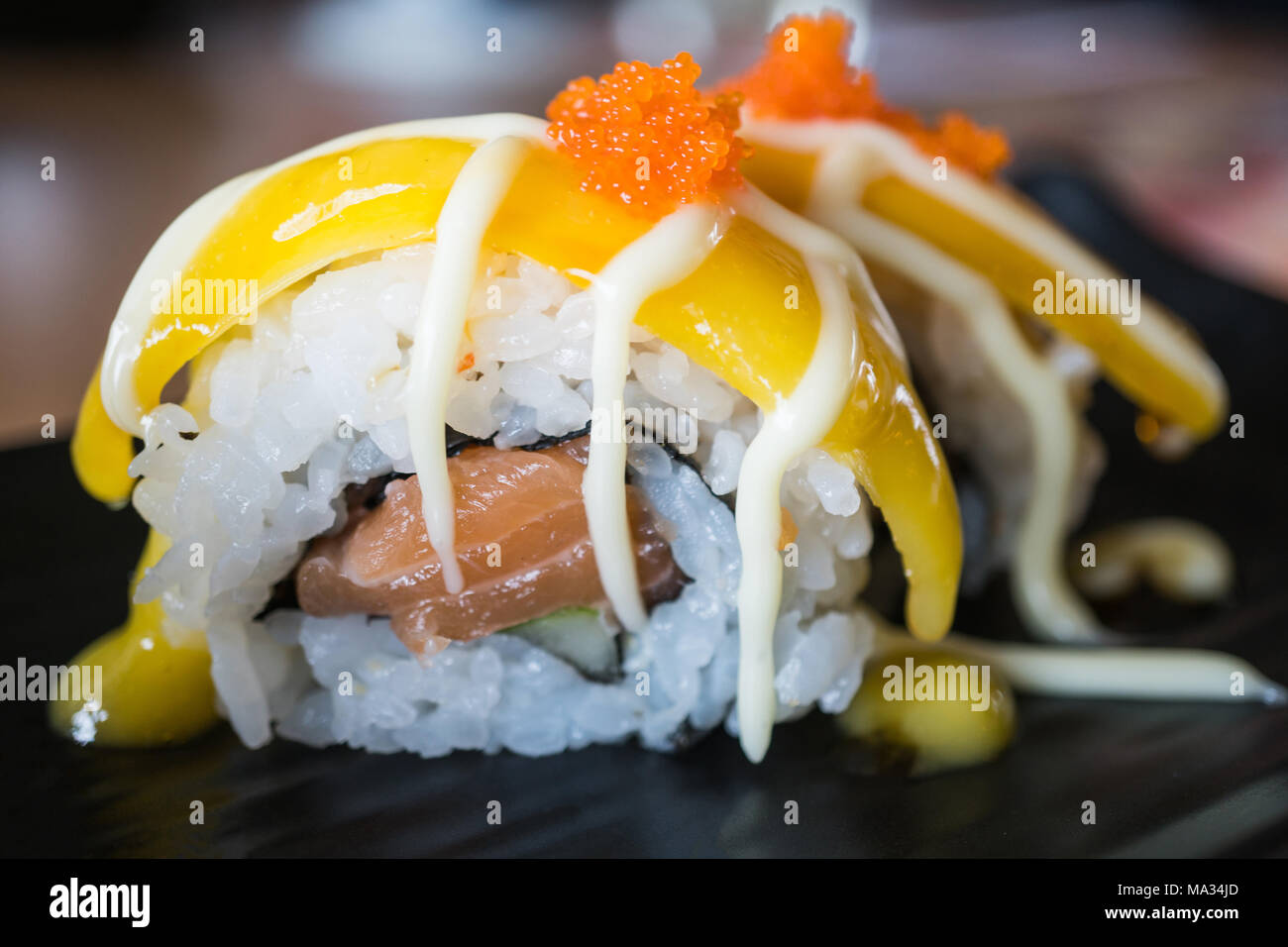 Rouleau de sushi de saumon à la mangue, fruits de la nourriture japonaise au style plat de céramique noire Banque D'Images