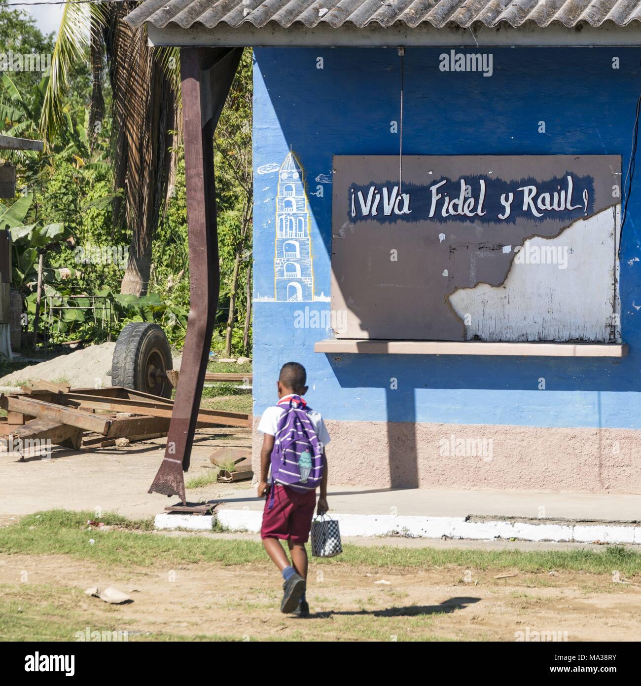 Un écolier fouines dans le soleil. Derrière lui se trouve le slogan "Vive Fidel et Raul !', peint sur le volet de la fenêtre d'une caserne à Manaca Iznaga dans la vallée des sucreries. (28 novembre 2017) | dans le monde entier Banque D'Images