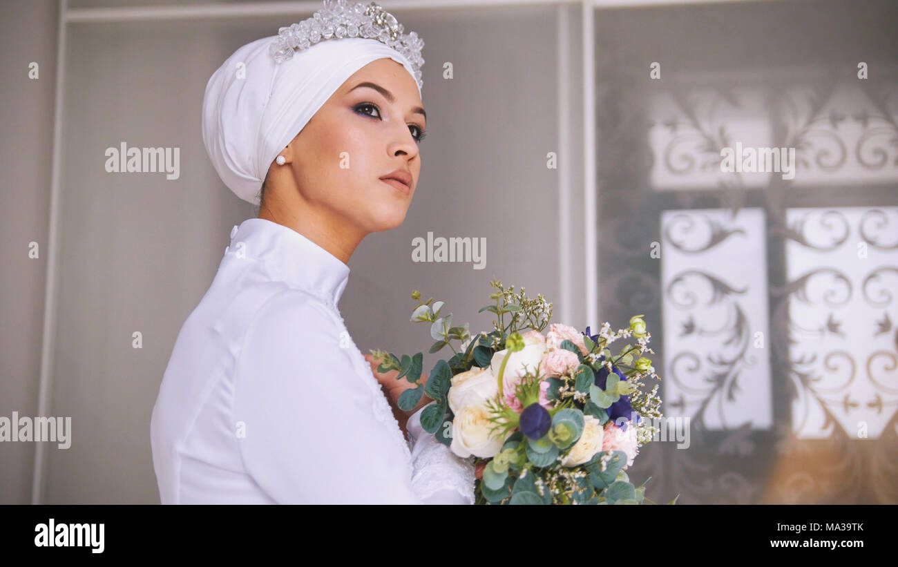 Belle Mariée musulmane avec les professionnels composent en robe de mariage avec bouquet de