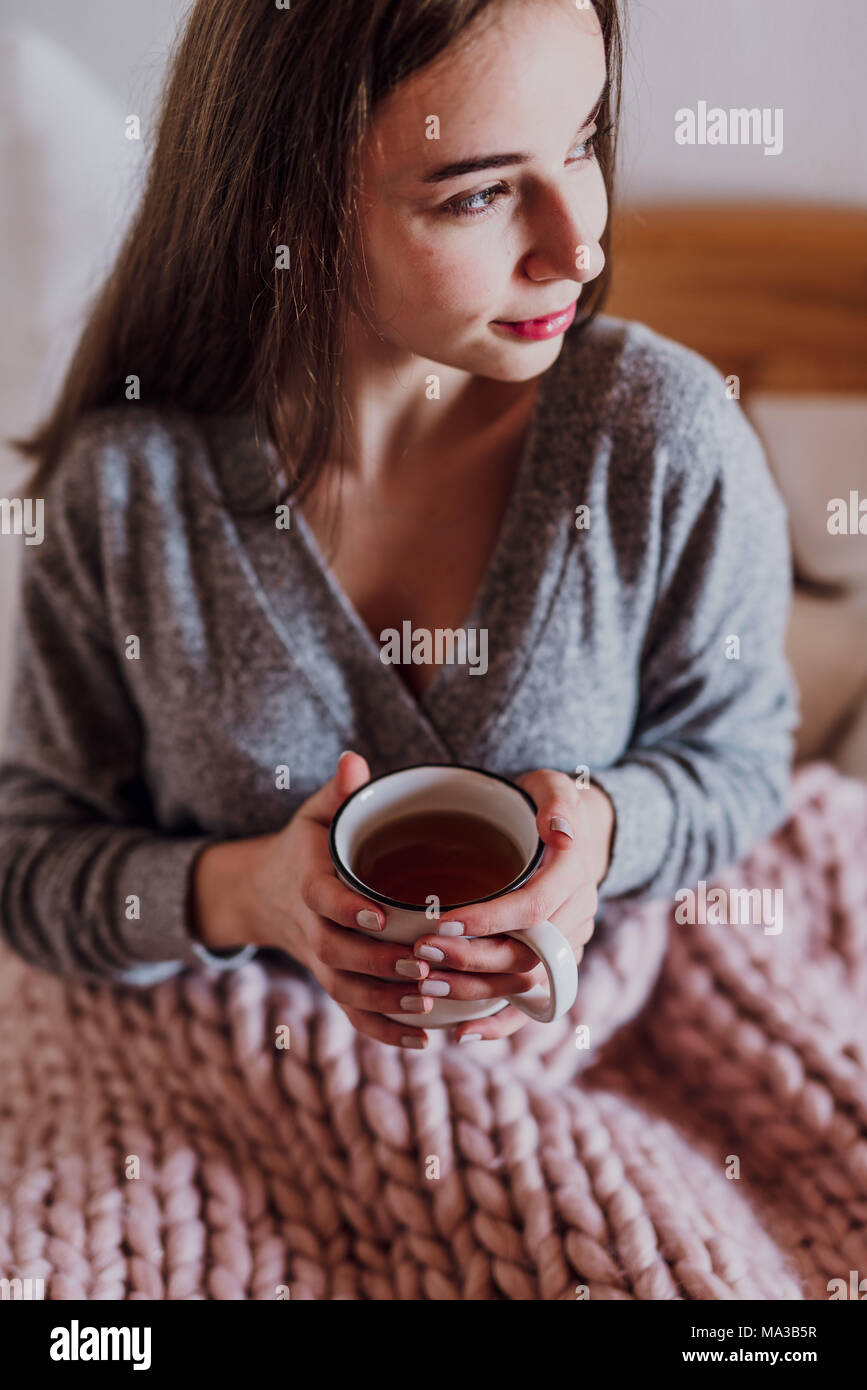 Jeune femme assise dans le lit avec une tasse de thé Banque D'Images
