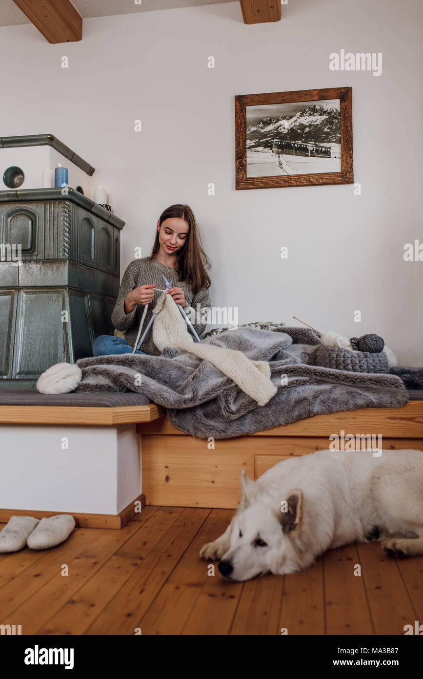 Jeune femme assise à côté d'un poêle en faïence et tricots,chien se trouve sur le sol Banque D'Images