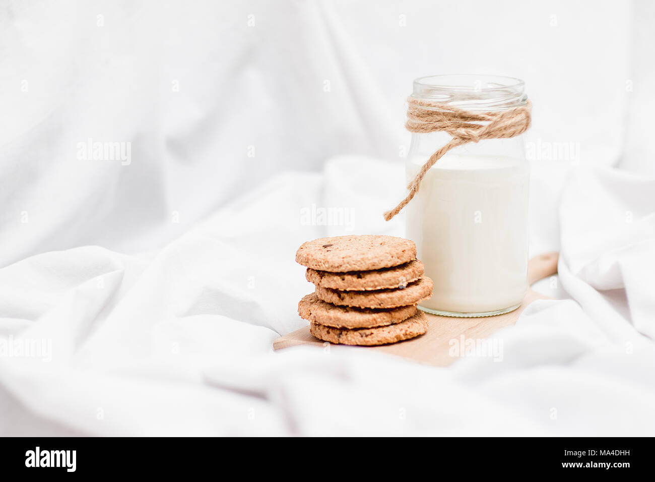 Photo d'un pot de lait et des biscuits sur une planche en bois sur un drap de lit Banque D'Images