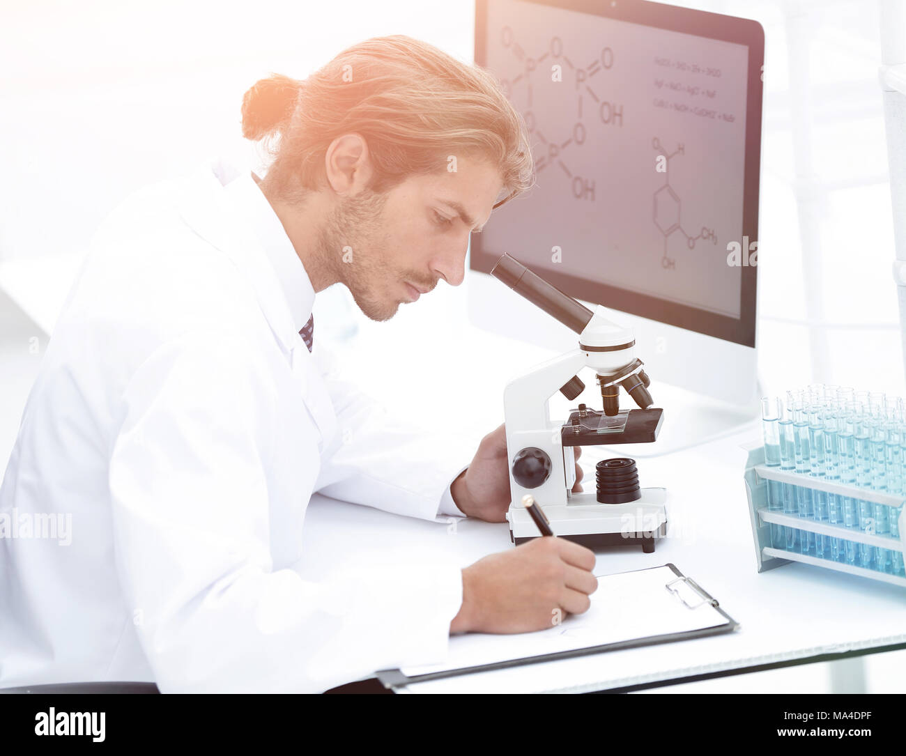 Un jeune chercheur ou spécialiste technique prend des notes dans le laboratoire d'histopathologie en utilisant un microscope optique et un ordinateur Banque D'Images
