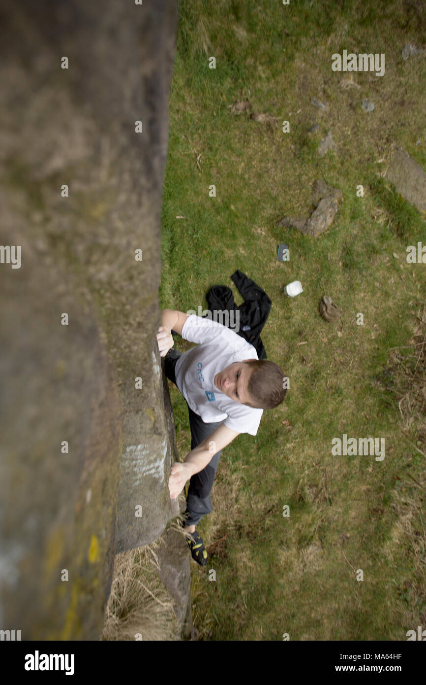 Jeune homme en escalade (bouldering) sans cordes sur rocher brunâtre. Banque D'Images