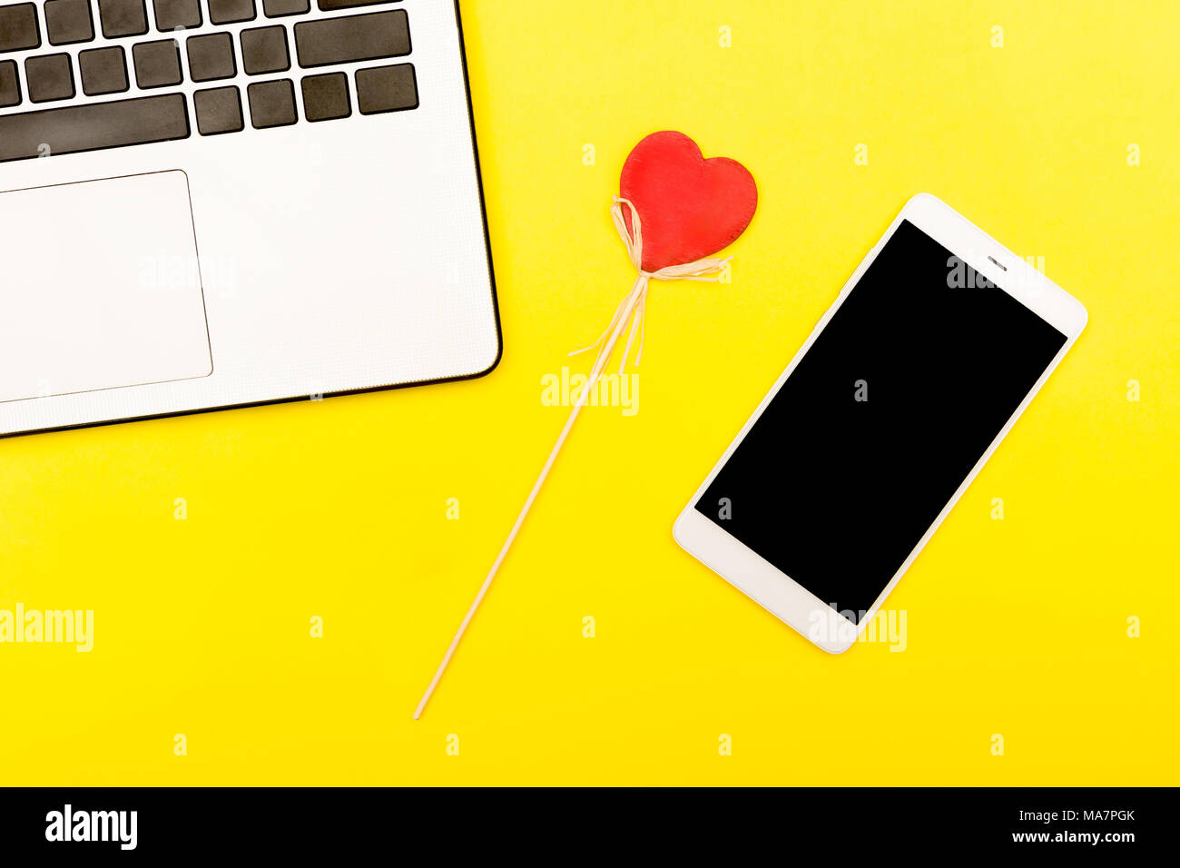 Symbole coeur d'un ordinateur portable smartphone. Un cœur décoratif sur un fond jaune avec smart gadgets. Banque D'Images