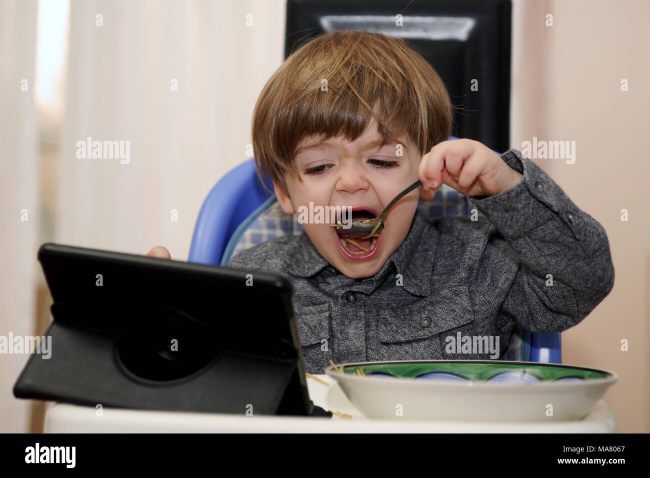 Jeune garçon regardant une tablette électronique tout en mangeant.Crédit : Mario Beauregard/Alamy Live News Banque D'Images