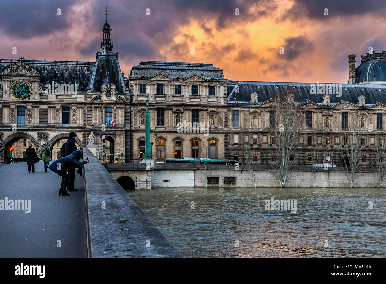 Couple de touristes prenant des photos sur le pont du Carrousel pont de Paris flanqué d'architecture du Louvre et un fiery sky au crépuscule Banque D'Images
