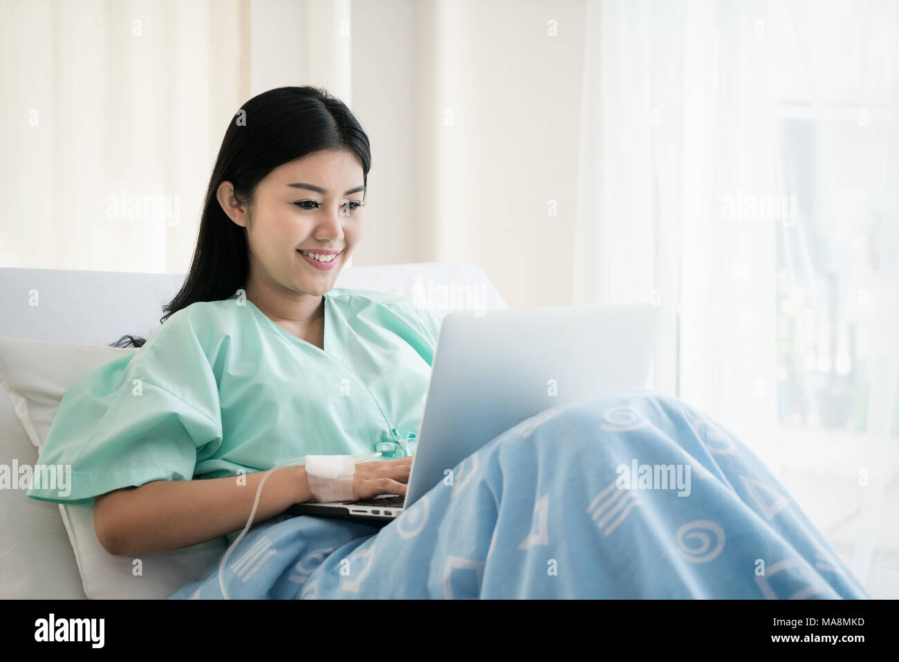 Asian woman malade couché dans un lit d'hôpital à l'aide d'un ordinateur portable pour se détendre lorsqu'elle un dédommagement pour les malades à l'hôpital. Banque D'Images