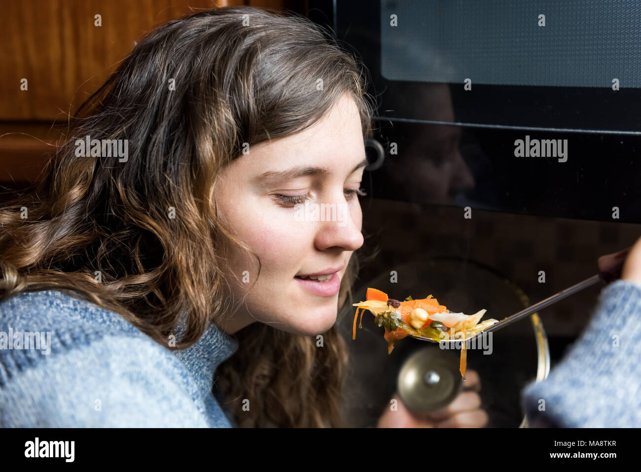Portrait de gros plan visage jeune femme essayant d'hiver chaud chaud maison soupe de légumes de spoon, bouche ouverte smiling in cold sweater Banque D'Images