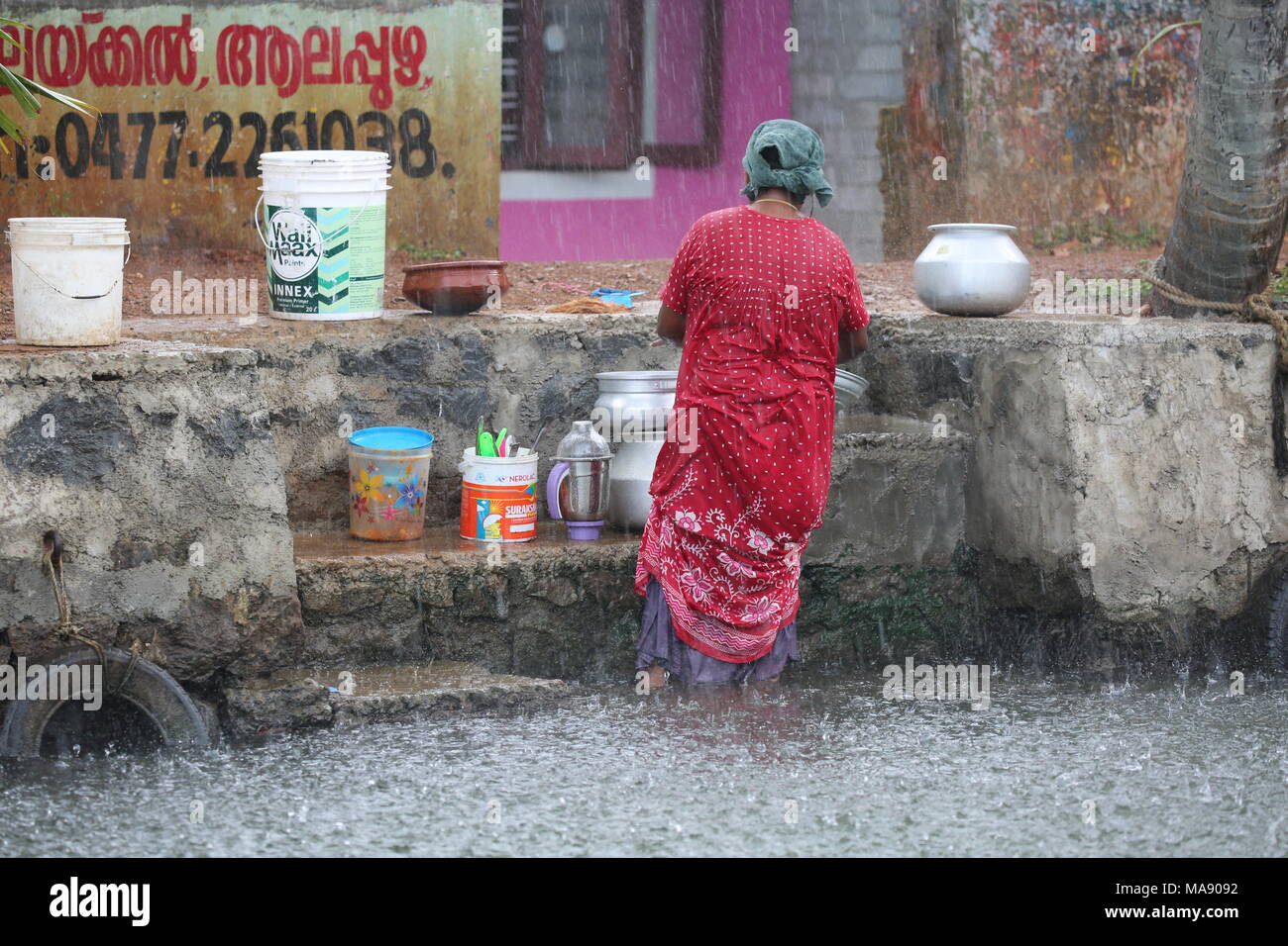 Vieille Femme indienne à laver les vêtements sur le bord de la rivière dans le Kerala - Alte Frau beim waschen von Kleidung im Regen stehend au Kerala - Inde du Sud Banque D'Images