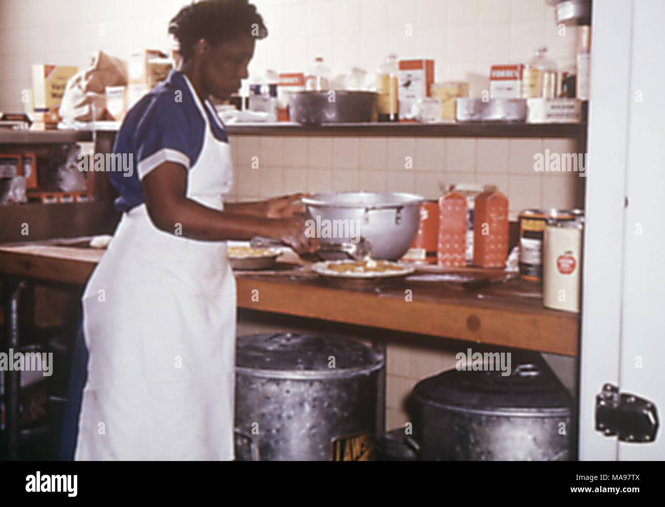 Photographie d'une femme préparant la nourriture dans la cuisine dans un camp de travail des travailleurs migrants, 1975. Image courtoisie CDC. () Banque D'Images