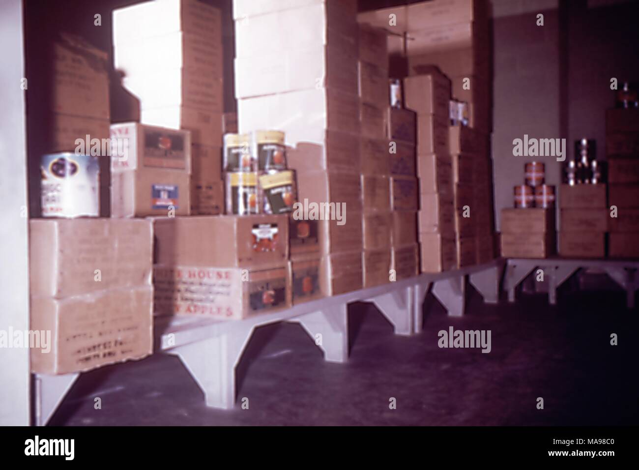 Photo d'une zone de stockage alimentaire intérieure à un camp de travail des travailleurs migrants, avec étagères bordées de boîtes en carton brun et de grandes boîtes de conserves de pommes, 1975. Image courtoisie CDC. () Banque D'Images