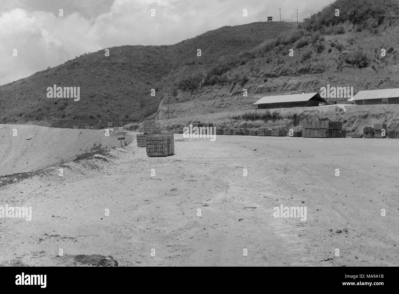 Photographie noir et blanc montrant une vue de fournitures empilés dans un paysage de sable, avec des casernes à droite et un poste d'observation sur une colline dans l'arrière-plan, photographié au Vietnam pendant la guerre du Vietnam, 1971. () Banque D'Images