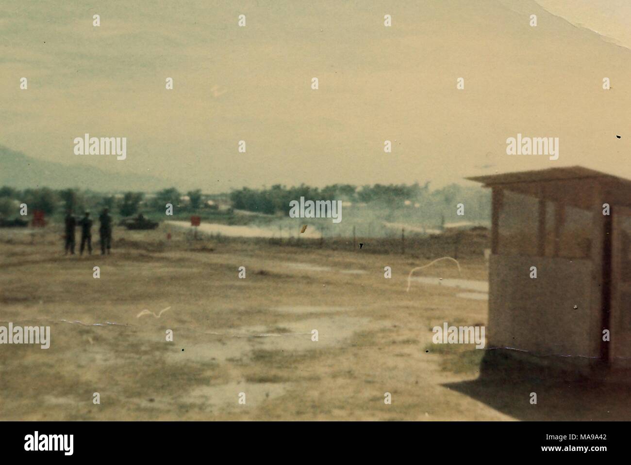 Photographie couleur montrant un poste de garde à la droite d'un champ boueux, avec trois chiffres (soldats sans doute) drapeaux, et un réservoir dans la distance, photographié au Vietnam pendant la guerre du Vietnam, 1968. () Banque D'Images