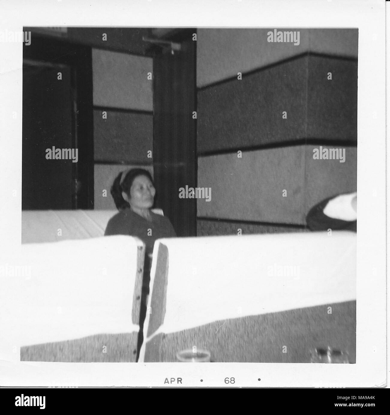 Photographie noir et blanc, d'une plus ancienne, femme asiatique, se penchant en arrière sur un siège dans une chambre avec des murs à rayures, avec une porte derrière elle et une barrière en face d'elle, photographié au Vietnam pendant la guerre du Vietnam (1955-1975), 1968. () Banque D'Images