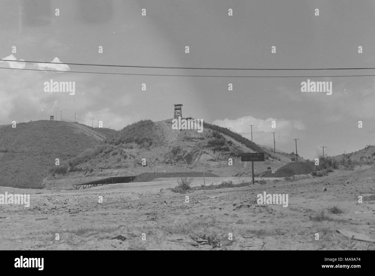 Photographie noir et blanc, montrant un paysage rocheux avec une route et ramada dans le plan intermédiaire, et deux collines en arrière-plan, chacune avec un poste d'observation en bois sur des échafaudages, photographié au Vietnam pendant la guerre du Vietnam (1955-1975), 1968. () Banque D'Images