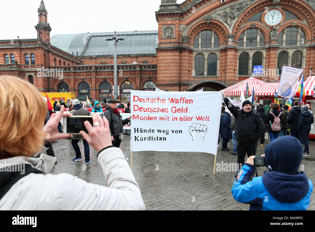 Bremen, Allemagne, 31 Mar 2018. Une femme et un petit garçon debout en face de la gare principale et de prendre des photos avec leurs téléphones mobiles d'une bannière avec le texte de l'armement Allemand Allemand - 'argent - Meurtre à travers le monde - Hands off Kurdistan" pendant le congé de Pâques Mars. Photo : Mohssen/Assanimoghaddam Crédit photo : dpa dpa alliance/Alamy Live News Banque D'Images