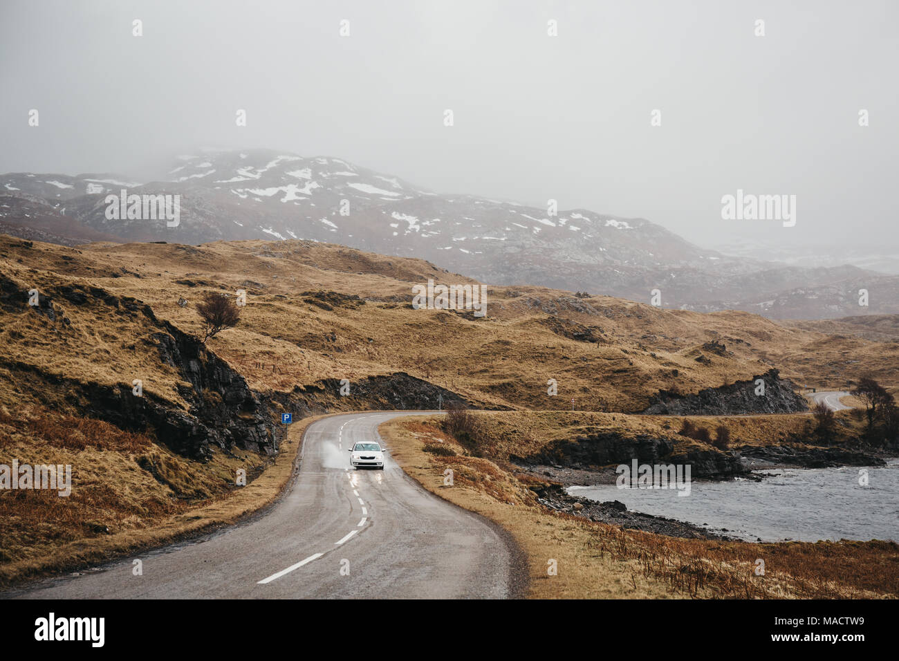 Voiture non identifié de la conduite sur une route à travers les Highlands écossais près de Lochinver brumeux sur une journée de printemps. Banque D'Images