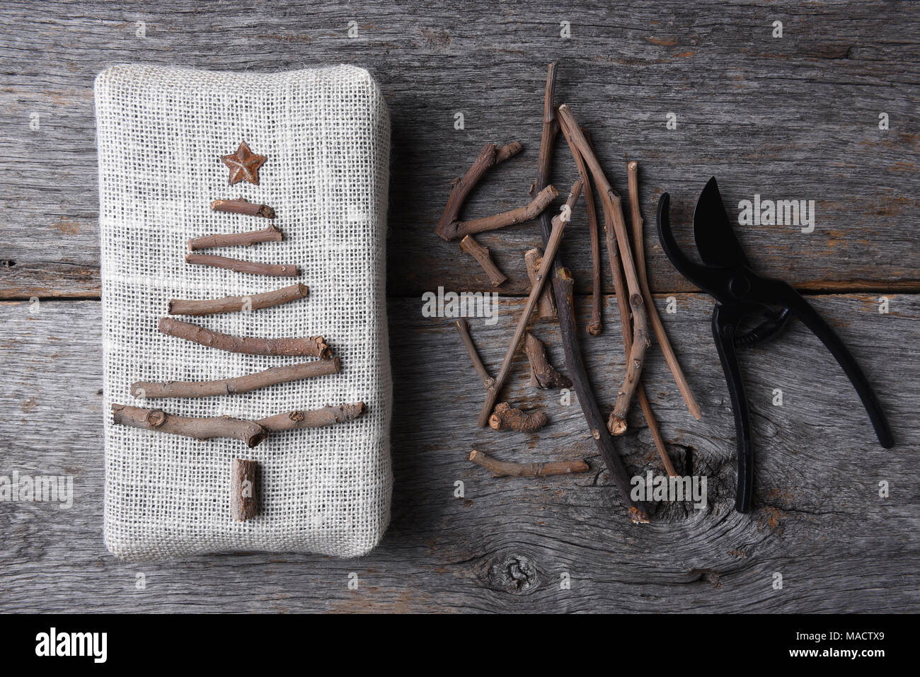 Passage tiré d'un cadeau de Noël enveloppé de toile avec une brindille arbre et star. Assortiment de brindilles et les cisaillements sont également sur la table de bois rustique. Banque D'Images