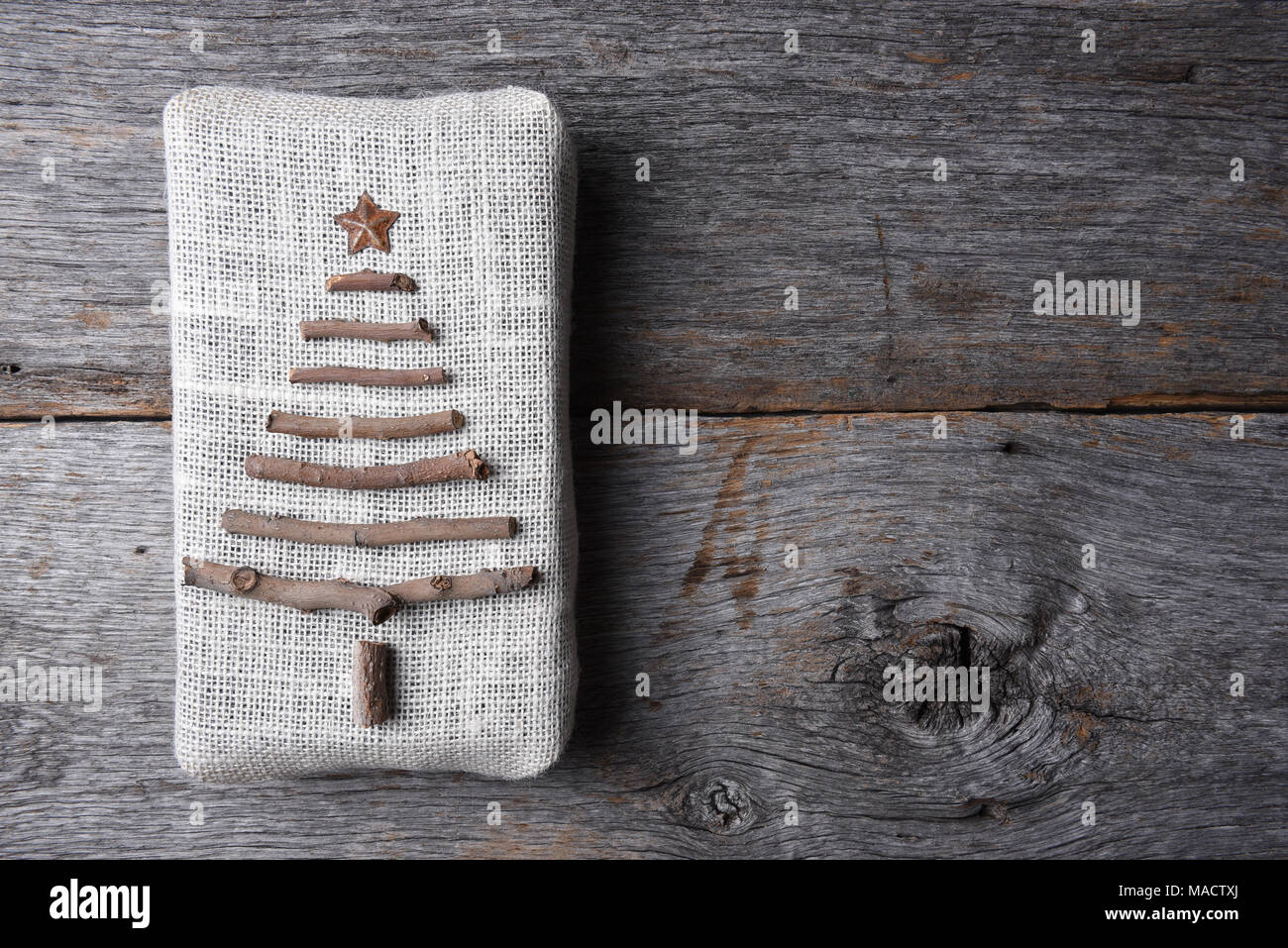 Passage tiré d'un cadeau de Noël enveloppé de toile avec une brindille arbre et star sur une table en bois rustique, avec l'exemplaire de l'espace. Banque D'Images
