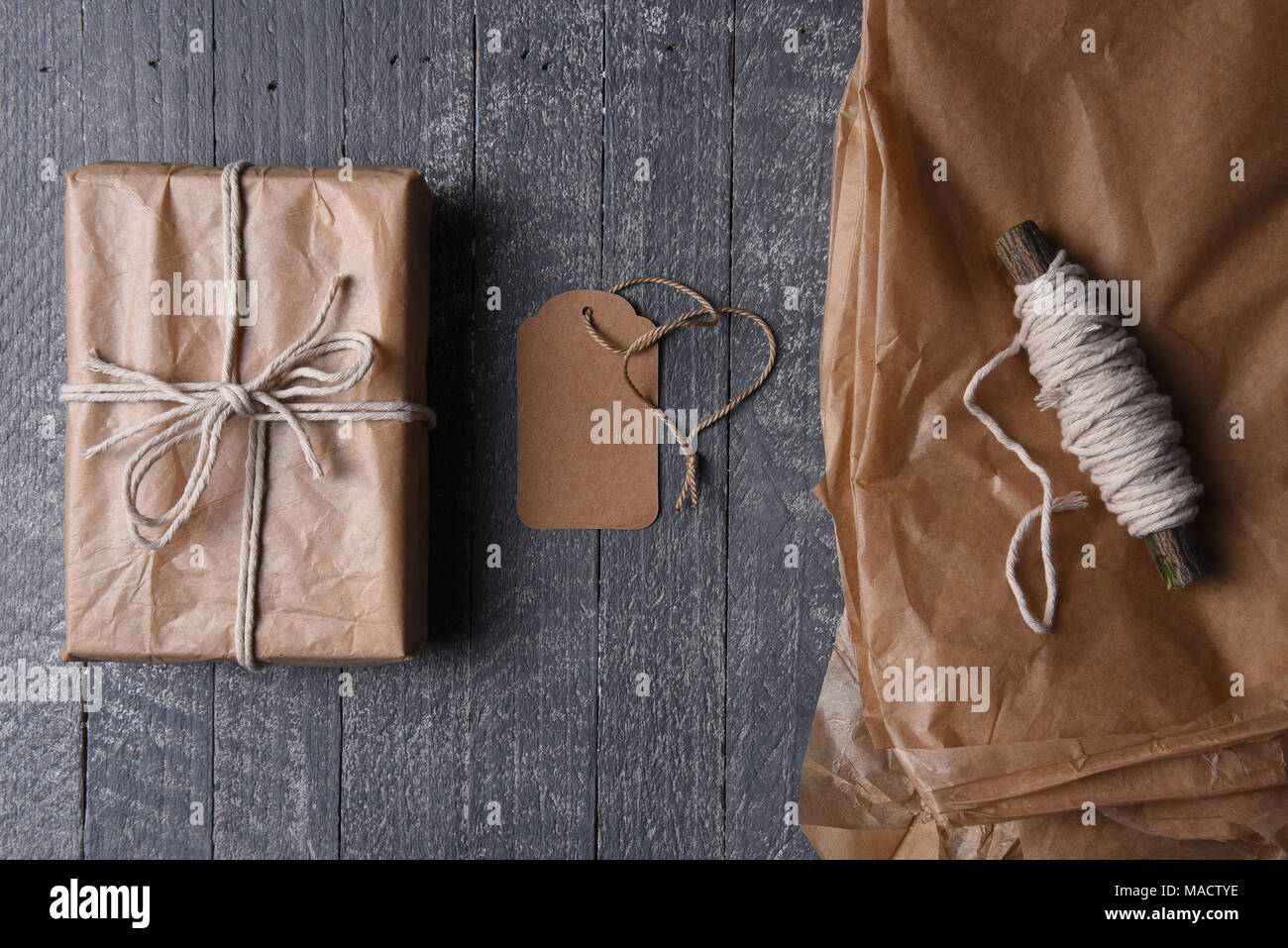 High angle shot de plain brown enveloppé dans du papier cadeau de Noël avec tag vierge et du papier supplémentaire et de la ficelle. Banque D'Images