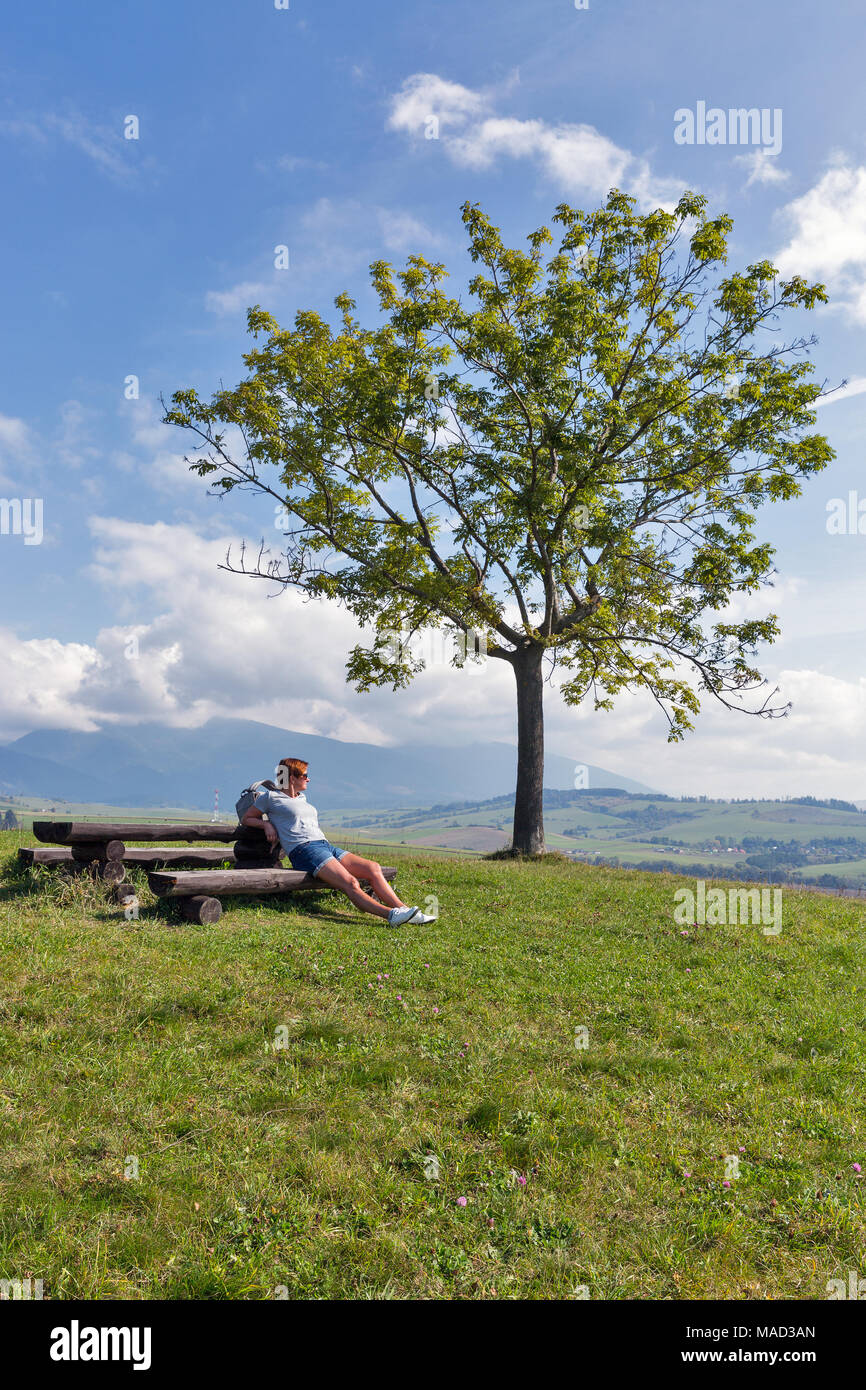 Portrait femme d'âge moyen ont un randonneur reste sur le banc en bois. Paysage de collines d'été près de Liptovsky Trnovec village de Slovaquie. Banque D'Images