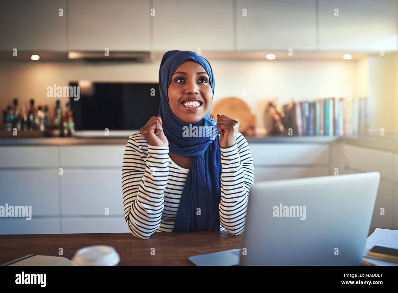 Jeune femme entrepreneur musulman extatique portant un hijab Célébrons les  succès tout en étant assis à une table dans sa cuisine et de travailler sur  un ordinateur portable Photo Stock - Alamy