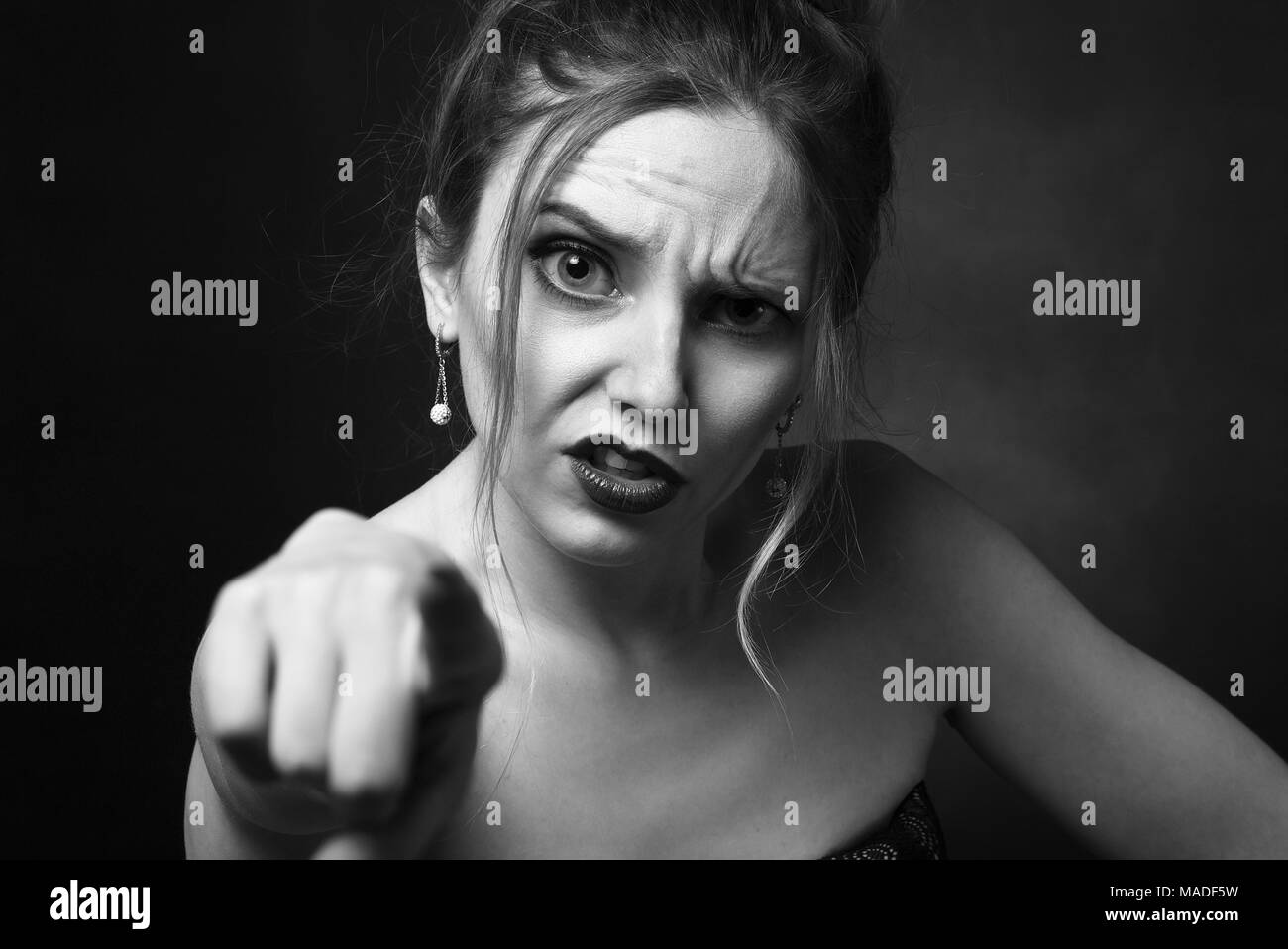 Jeune femme en colère sur fond noir point sur appareil photo, monochrome Banque D'Images