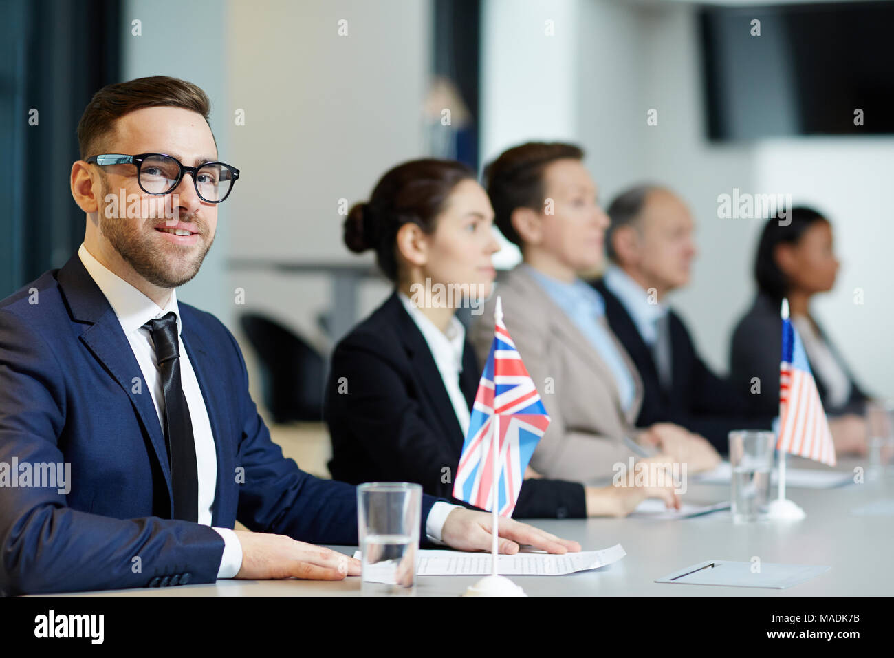 En fonction de délégué élégant et de lunettes à la recherche à huis clos à conférence politique sur fond d'autres participants Banque D'Images