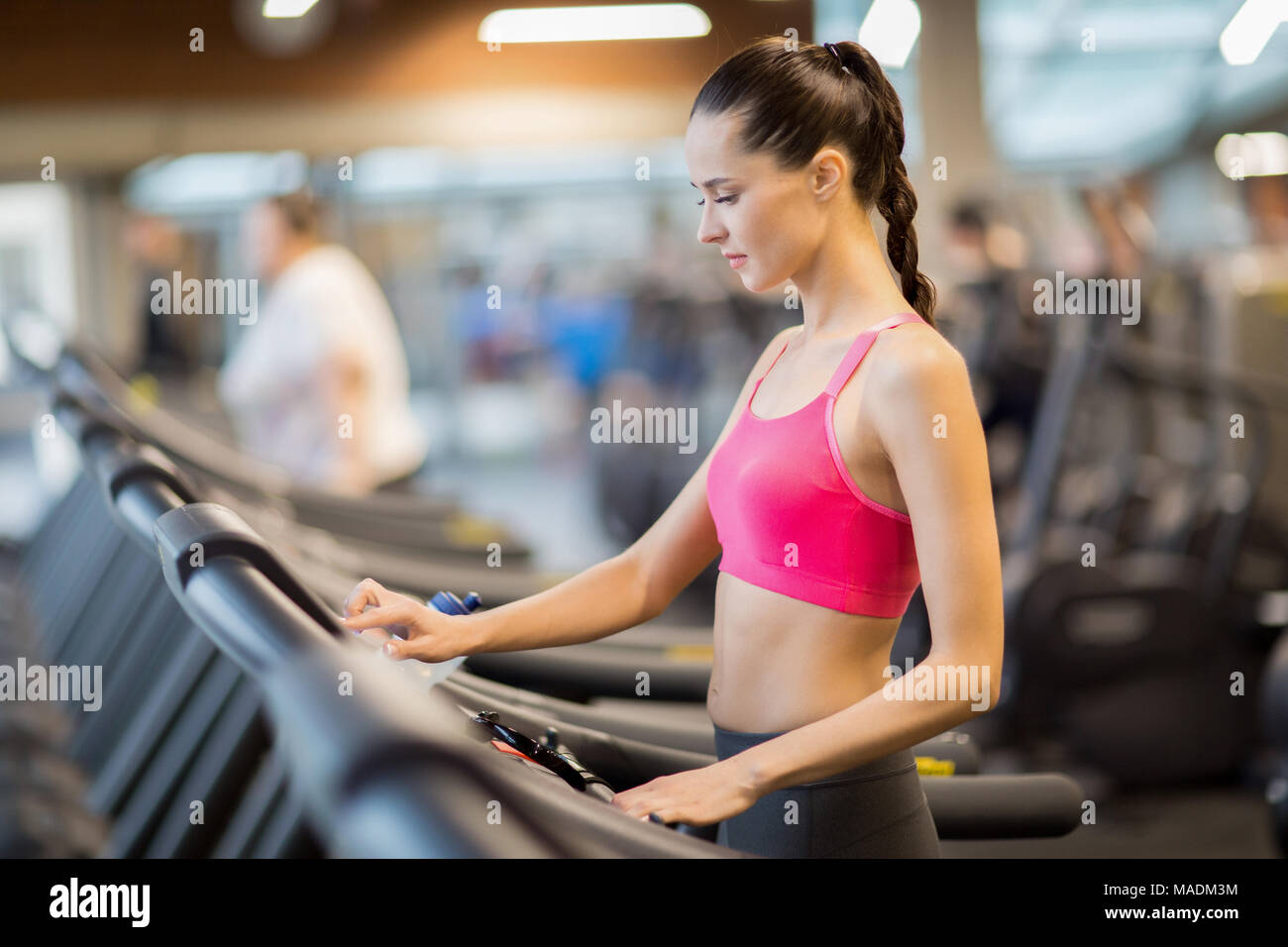 Fit girl dans activewear en choisissant Exécuter la vitesse affichée en allant faire de l'exercice sur tapis roulant dans une salle de sport Banque D'Images