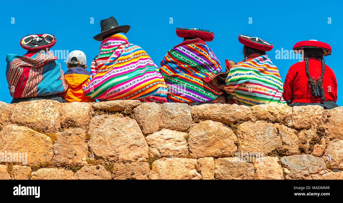 Un groupe de femmes autochtones Quechua péruvienne en costume traditionnel avec un garçon assis sur un ancien mur Inca à Chincheros près de Cusco, ville du Pérou. Banque D'Images