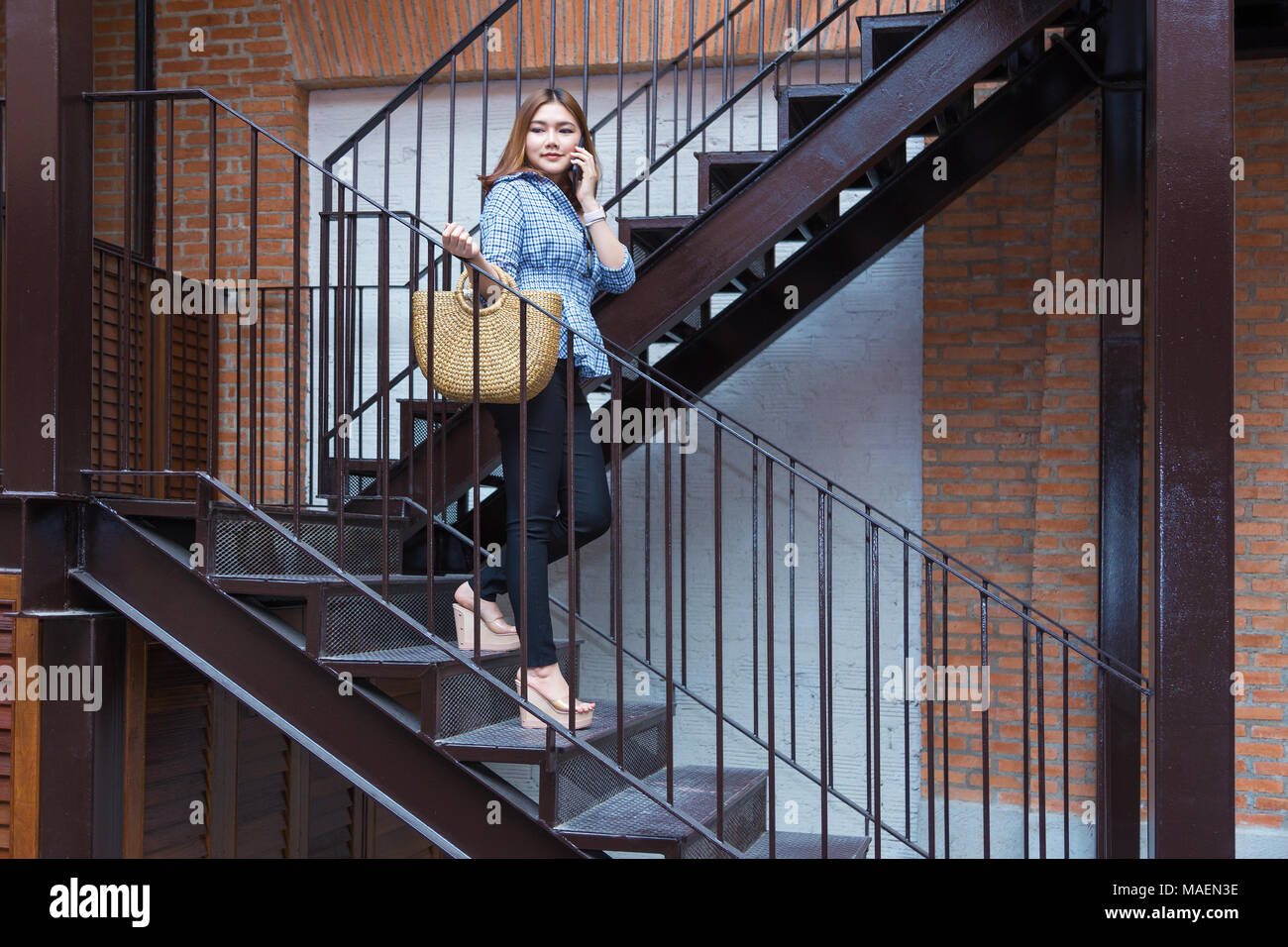 Young Asian woman going shopping descendant les escaliers d'un centre commercial tout en parlant à son téléphone intelligent Banque D'Images
