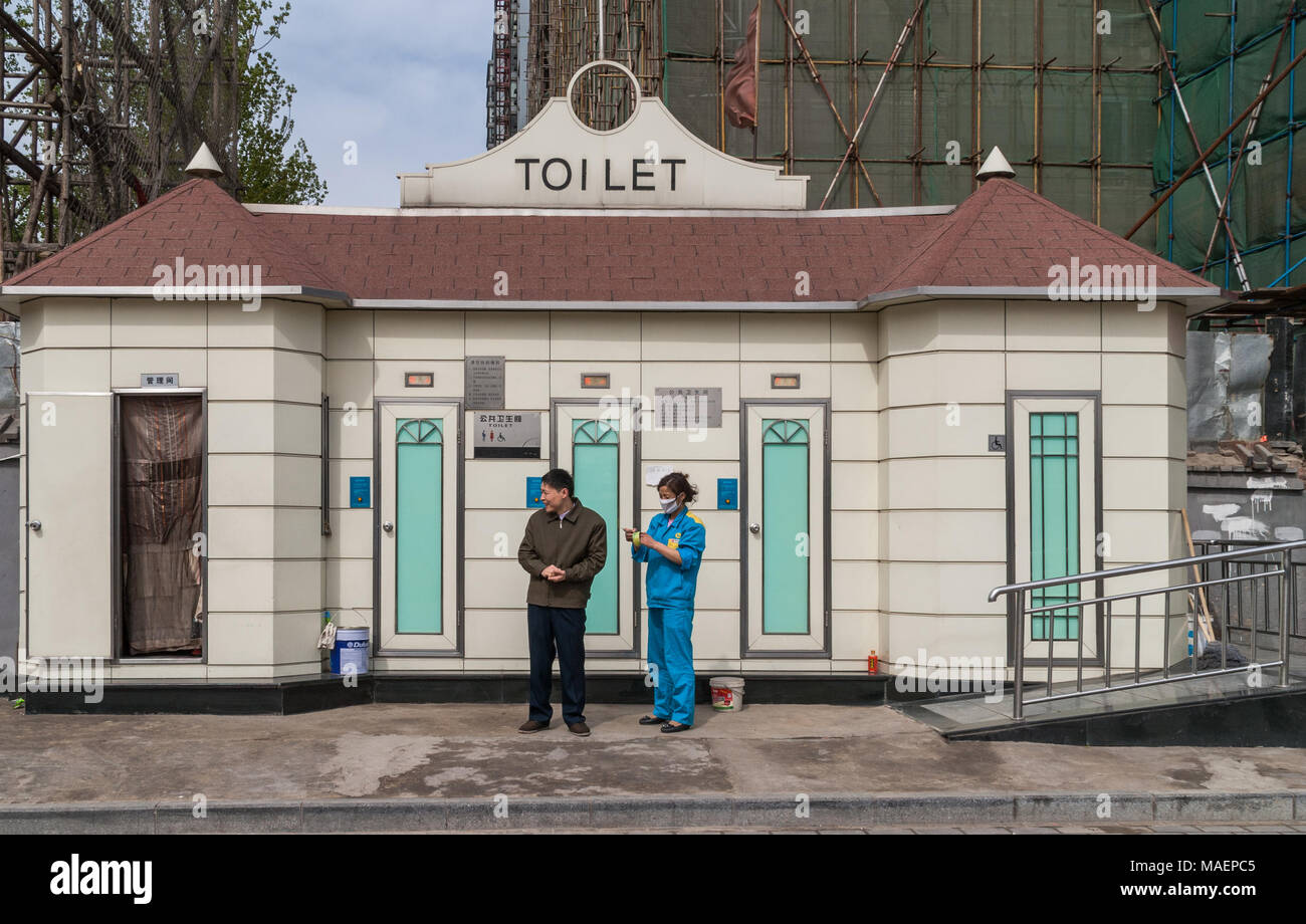 Beijing, Chine - le 26 avril 2010 : Neat avec toit beige marron moderne cabine des toilettes publiques le long de la rue. Ouvrier d'entretien dans l'uniforme bleu sur place. Je l'homme Banque D'Images