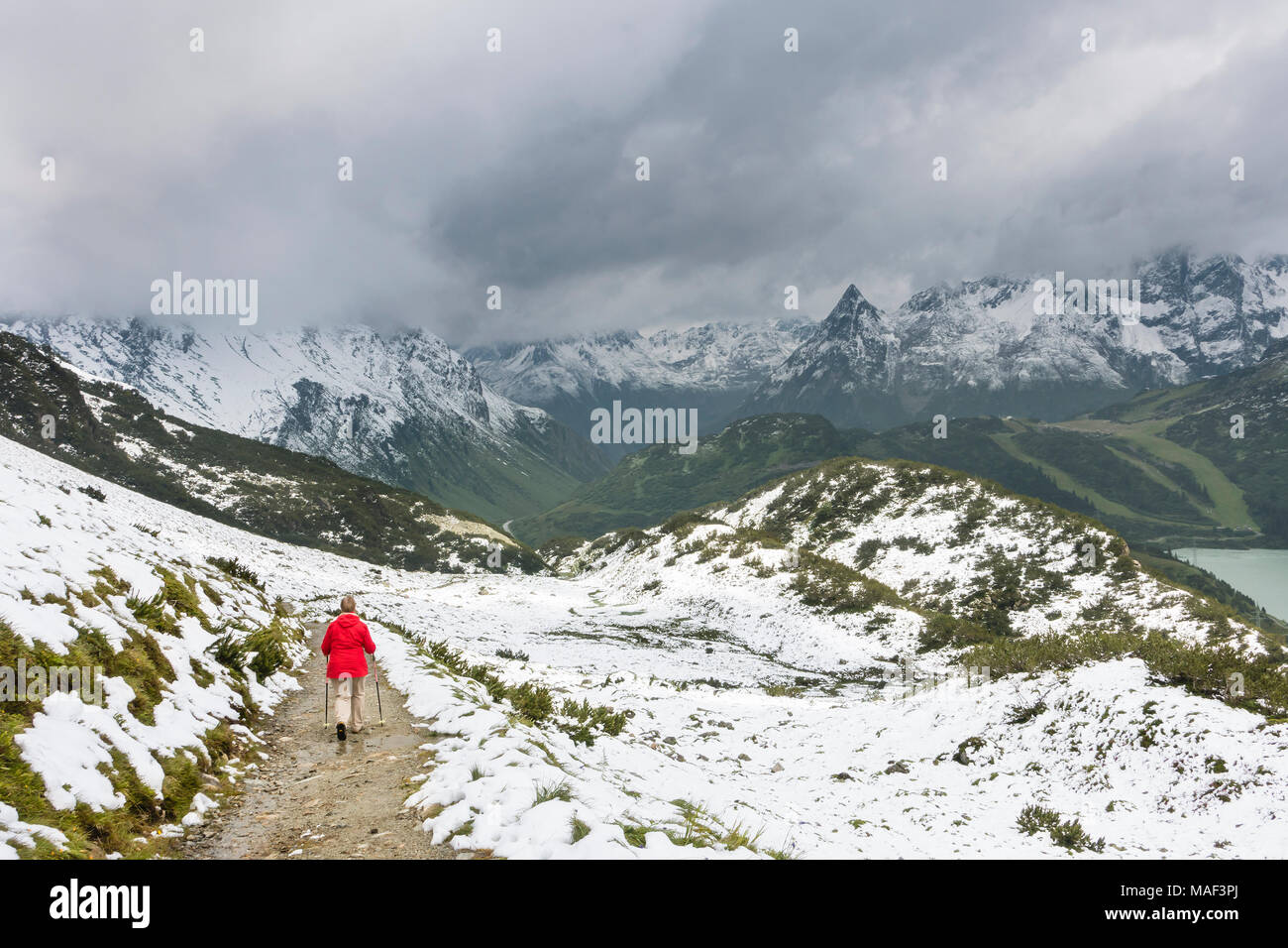 Une femme portant un randonneur hauts manteau rouge de la randonnée dans la neige en été sur le chemin de l'Zeinisjoch dans la vallée de Paznaun près de Galtur en Autriche. L Banque D'Images