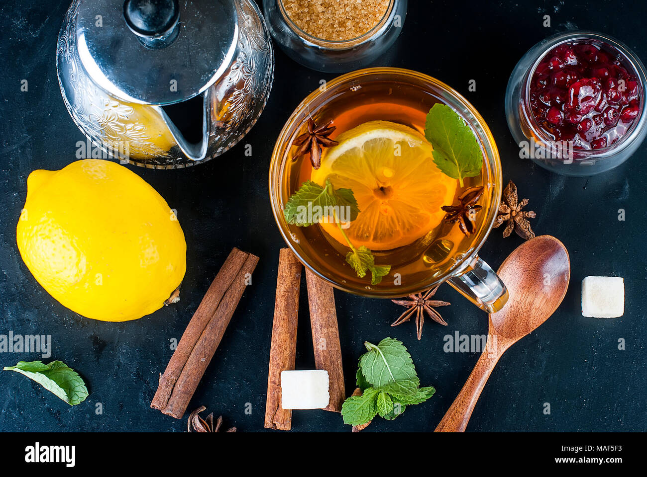 Automne thé chaud avec du citron, de la menthe dans une tasse en verre et la confiture de framboises sur un fond noir, l'espace de copie. Banque D'Images