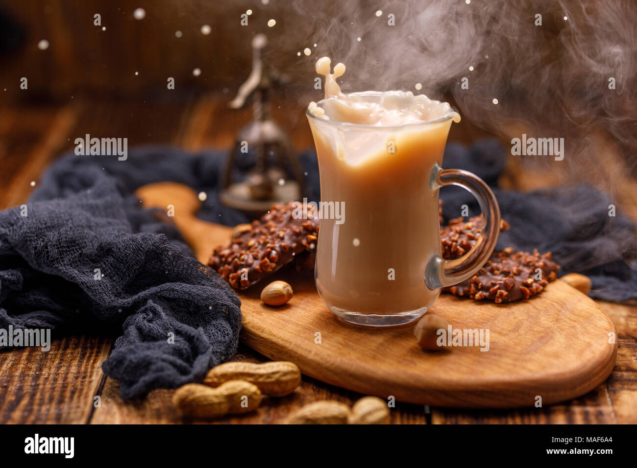 Tabac, thé au lait et biscuits au chocolat avec des noix pour le petit-déjeuner est renversé à partir de la tasse. Thé avec des biscuits dans une tasse en verre avec une éclaboussure. Banque D'Images
