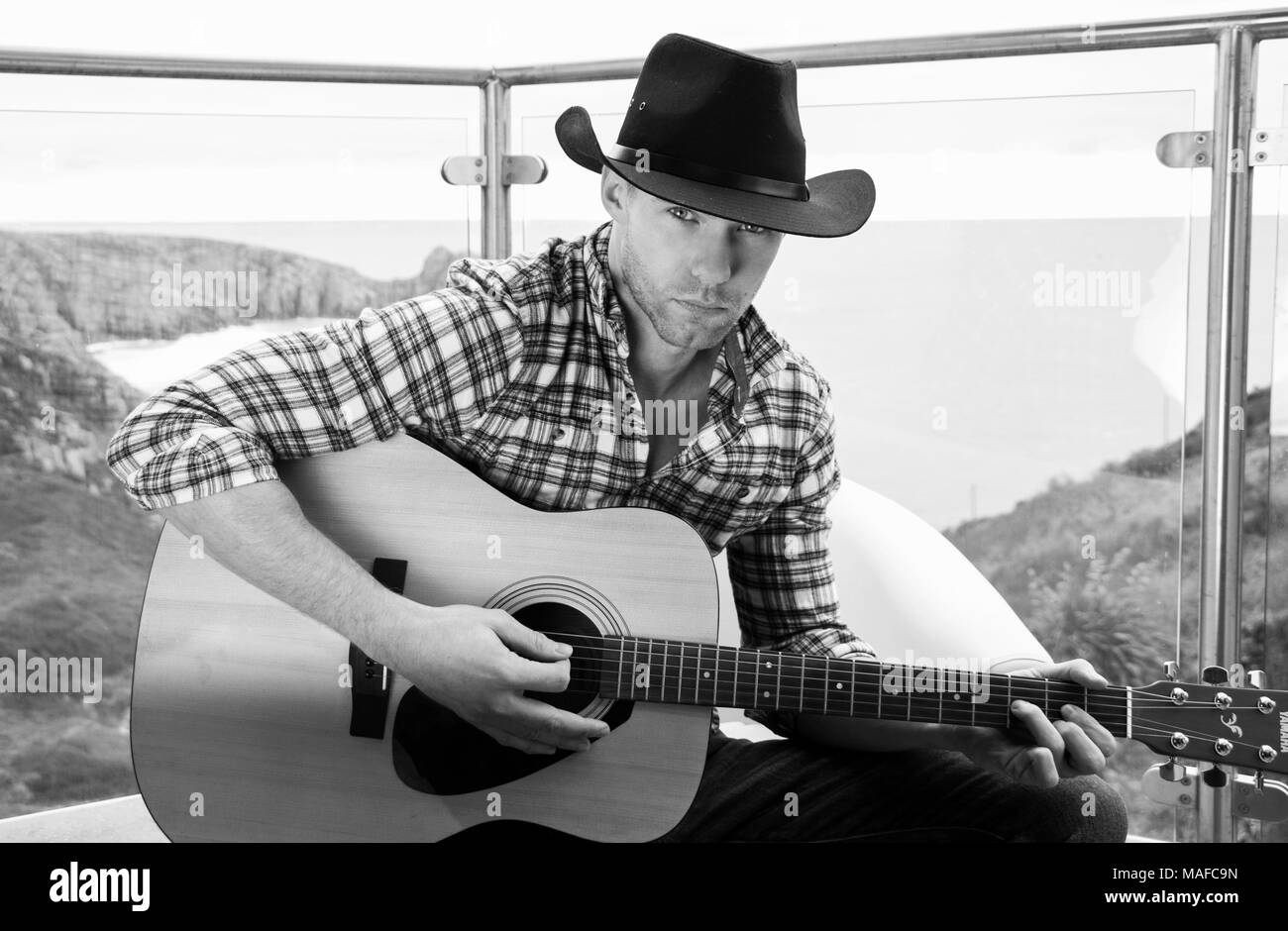 Beau cowboy country et western singer wearing hat et à jouer de la guitare sur l'hôtel balcon donnant sur l'océan en arrière-plan Banque D'Images