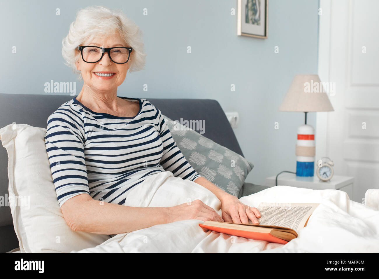 Grand-mère lit un livre avec des lunettes au lit. Piscine, studio, tournage  intérieur chambre à coucher Photo Stock - Alamy