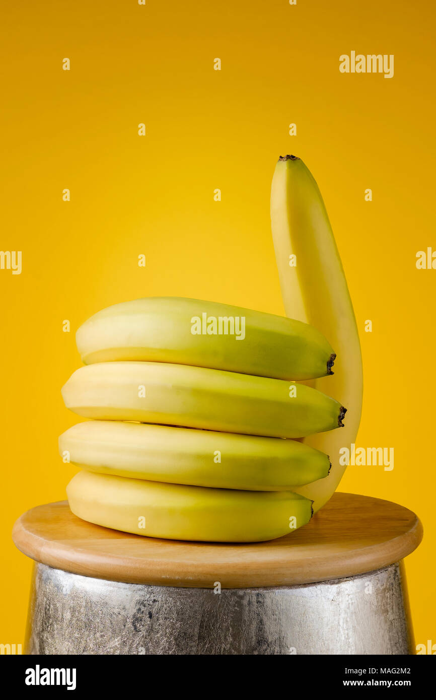 La banane est posé sur une planche en bois en forme de main avec le pouce vers le haut, sur un fond jaune comme nous, saine food concept. Banque D'Images