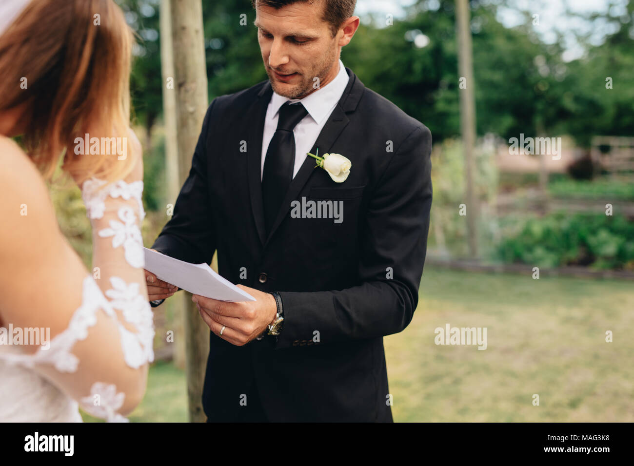 Beau jeune marié lisant des vœux de mariage dans un journal. rituels de cérémonie de mariage d'un couple dans le parc. Banque D'Images Beau jeune marié lisant des vœux de mariage dans un journal. rituels de cérémonie de mariage d'un couple dans le parc. Banque D'Images