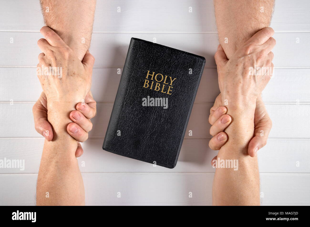 Vieil Homme et femme tenant les mains autour d'une Sainte Bible sur blanc bois board Banque D'Images