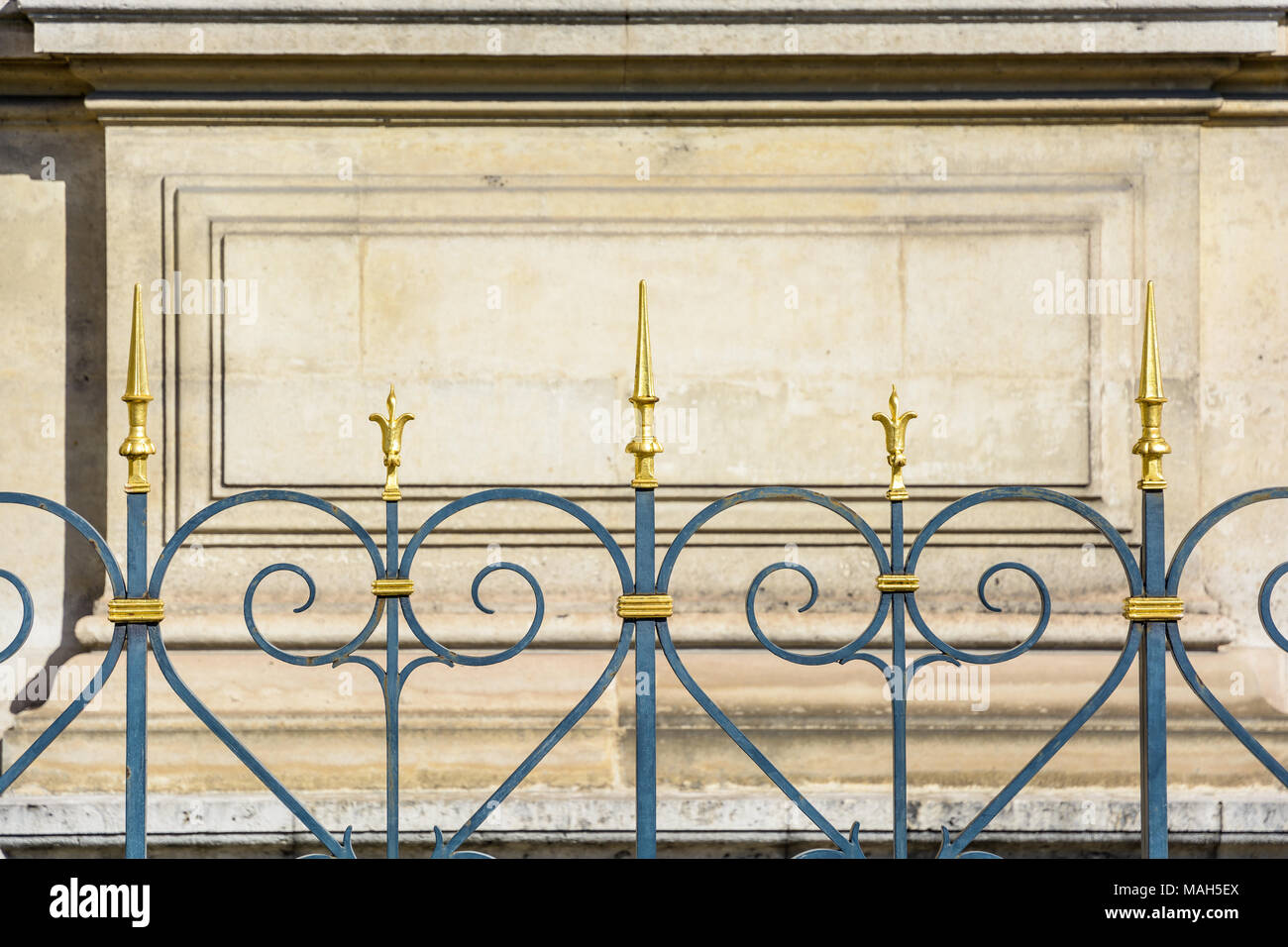 Vue de face d'une solide clôture en fer forgé noir surmontée de pointes dorées et d'une fleur de lis longeant un bâtiment historique à Paris, en France. Banque D'Images